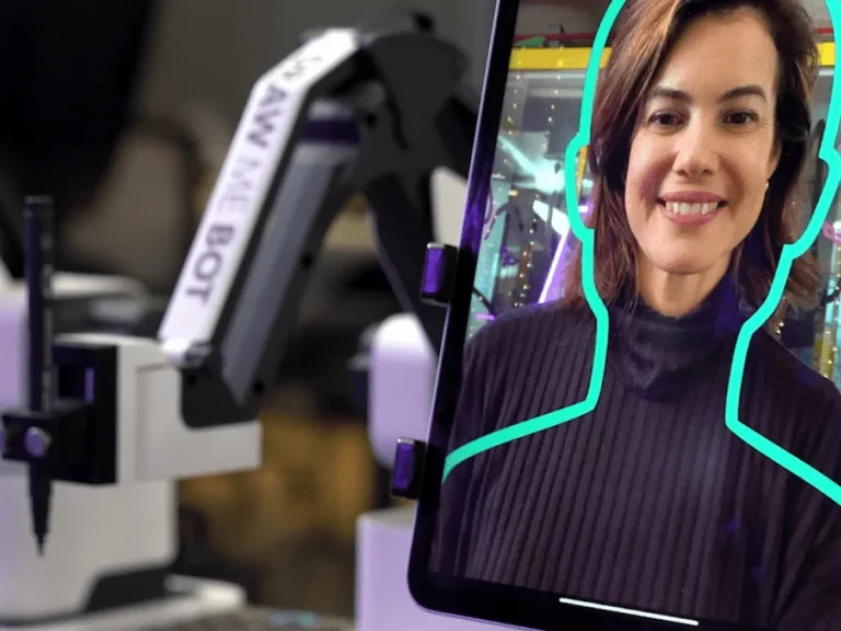 Robot arm holding a pen beside a tablet that shows a smiling woman inside a head-and-shoulders outline